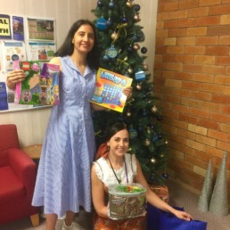 Student and teacher holding Christmas gift donations by Christmas Tree