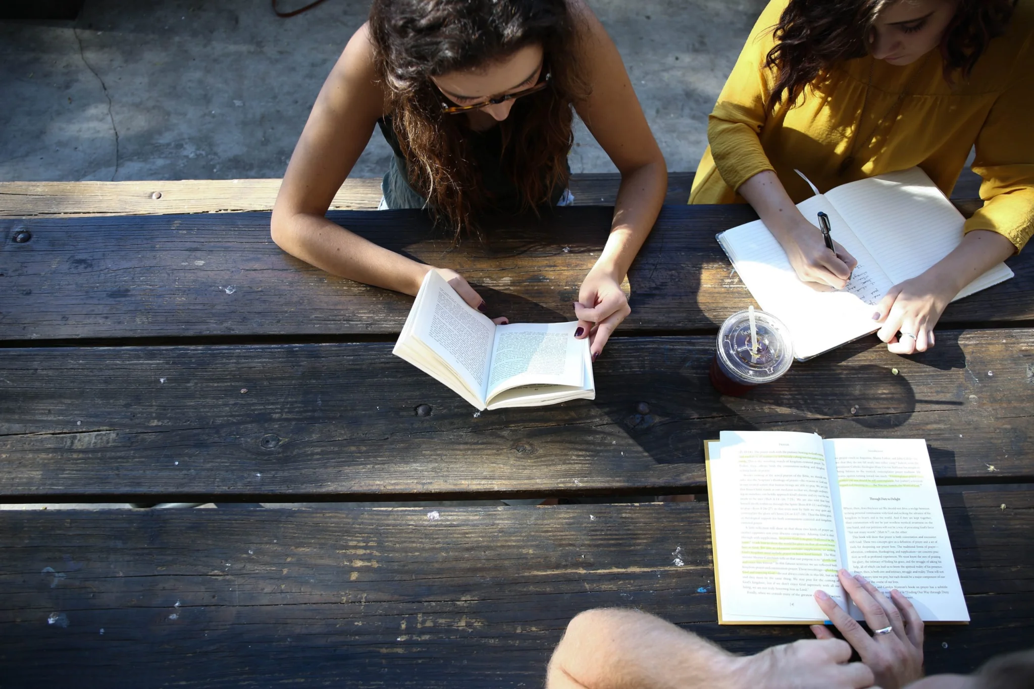 Three women sitting on an outdoor table whilst reading and writing