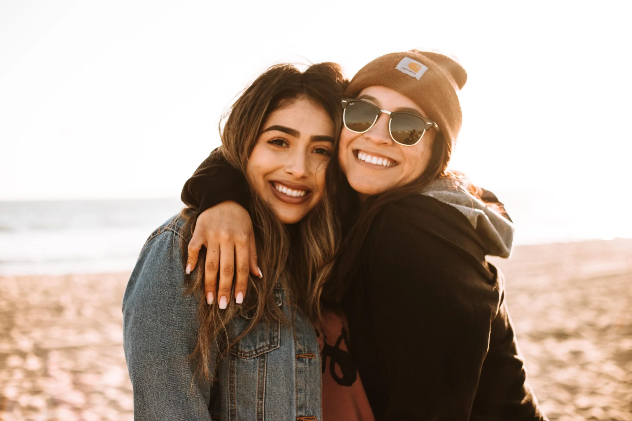 Two young adult women hugging and smiling on the beach
