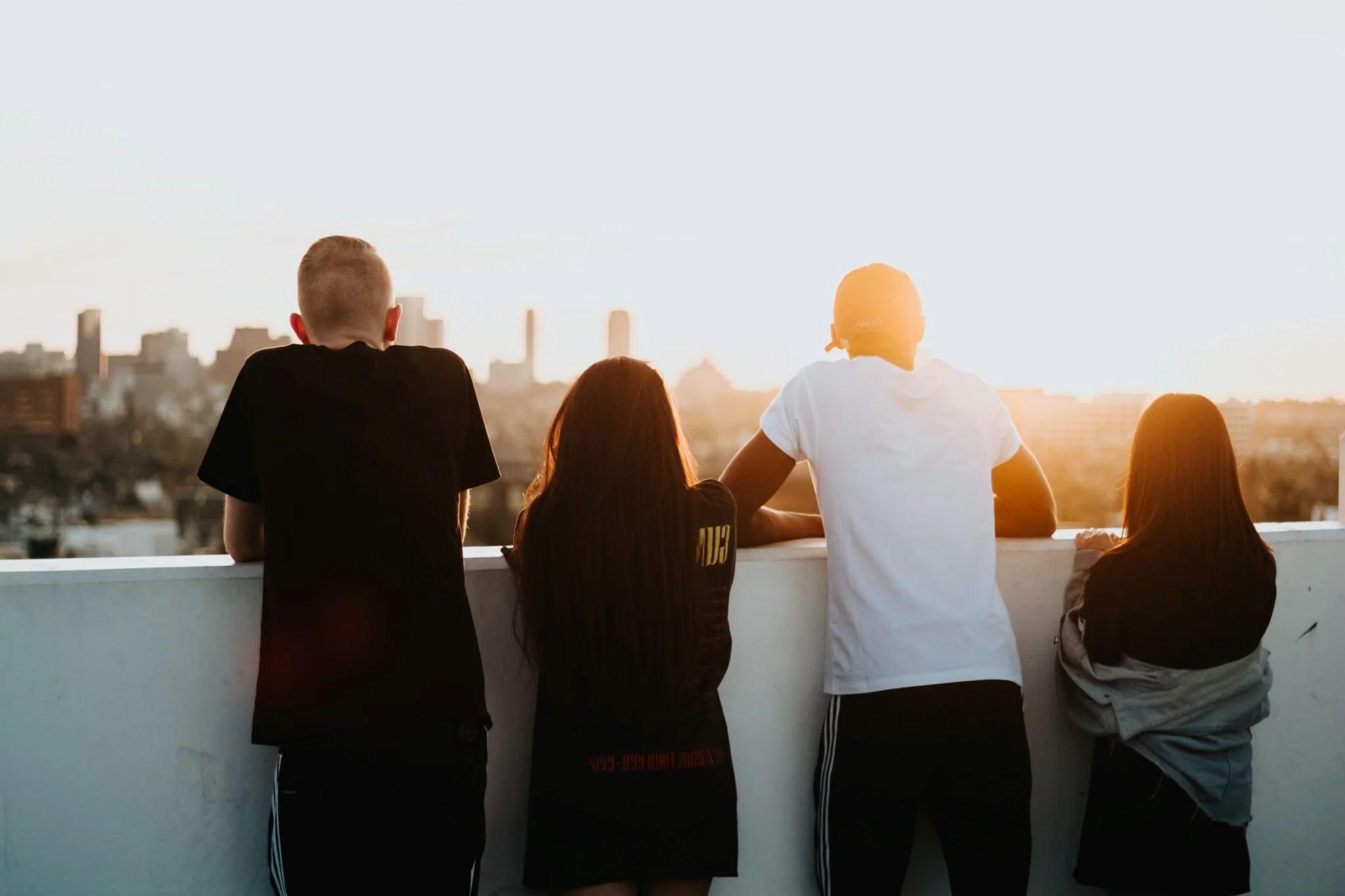 Four young adults leaning over a ledge watching the sun set