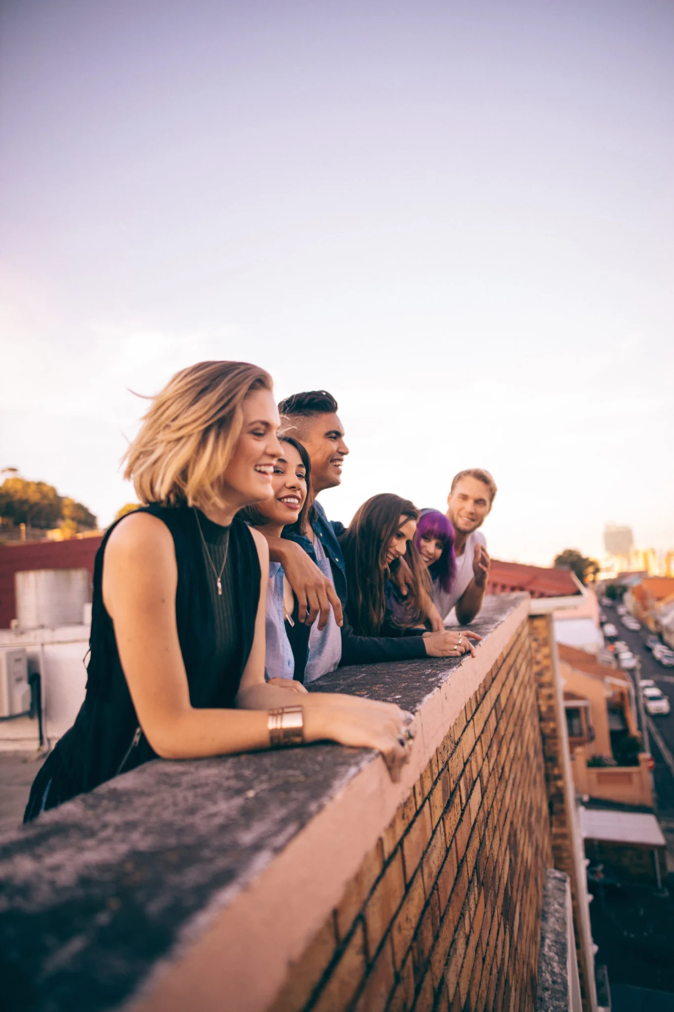 Group of multi-ethnic teenager friends leaning on the parapet of a rooftop laughing and chatting